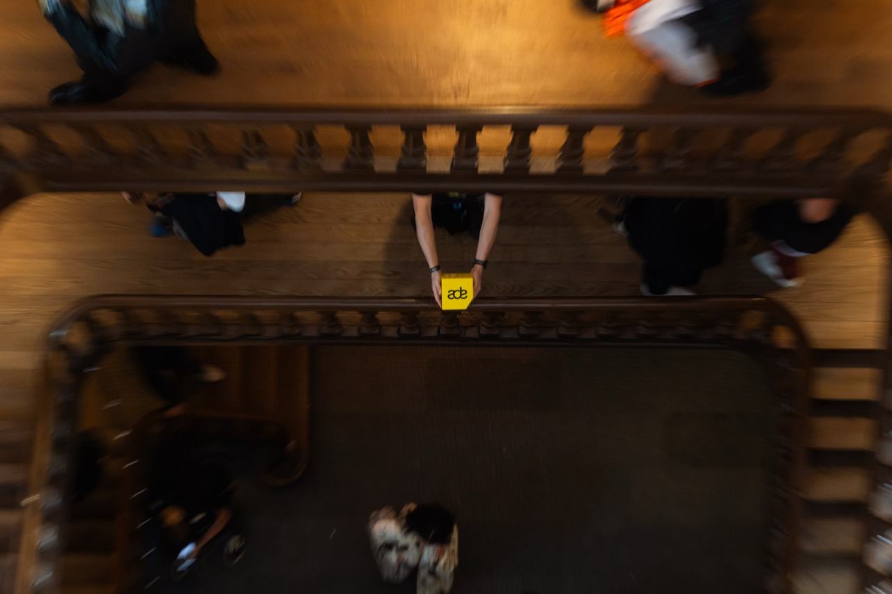 Looking down the stairwell at Felix in Amsterdam during ADE 2025; someone on the landing holds up the yellow ADE cube